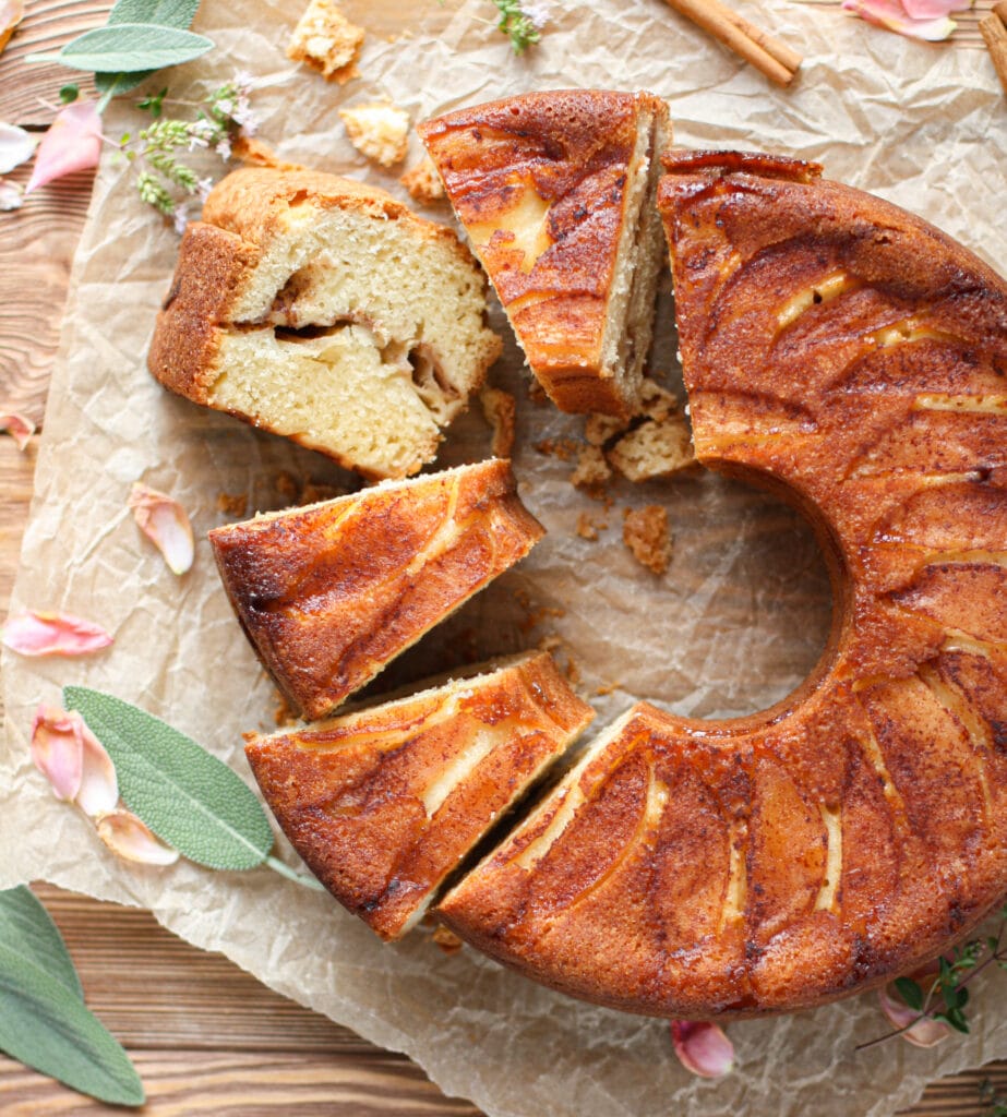 Jewish Apple Cake partially cut into slices and garnished with sage leaves