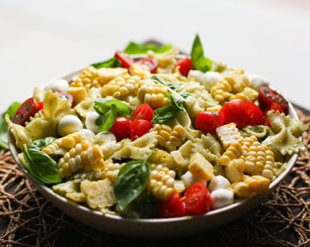 Sideways view of pesto pasta salad with fresh tomatoes and corn 