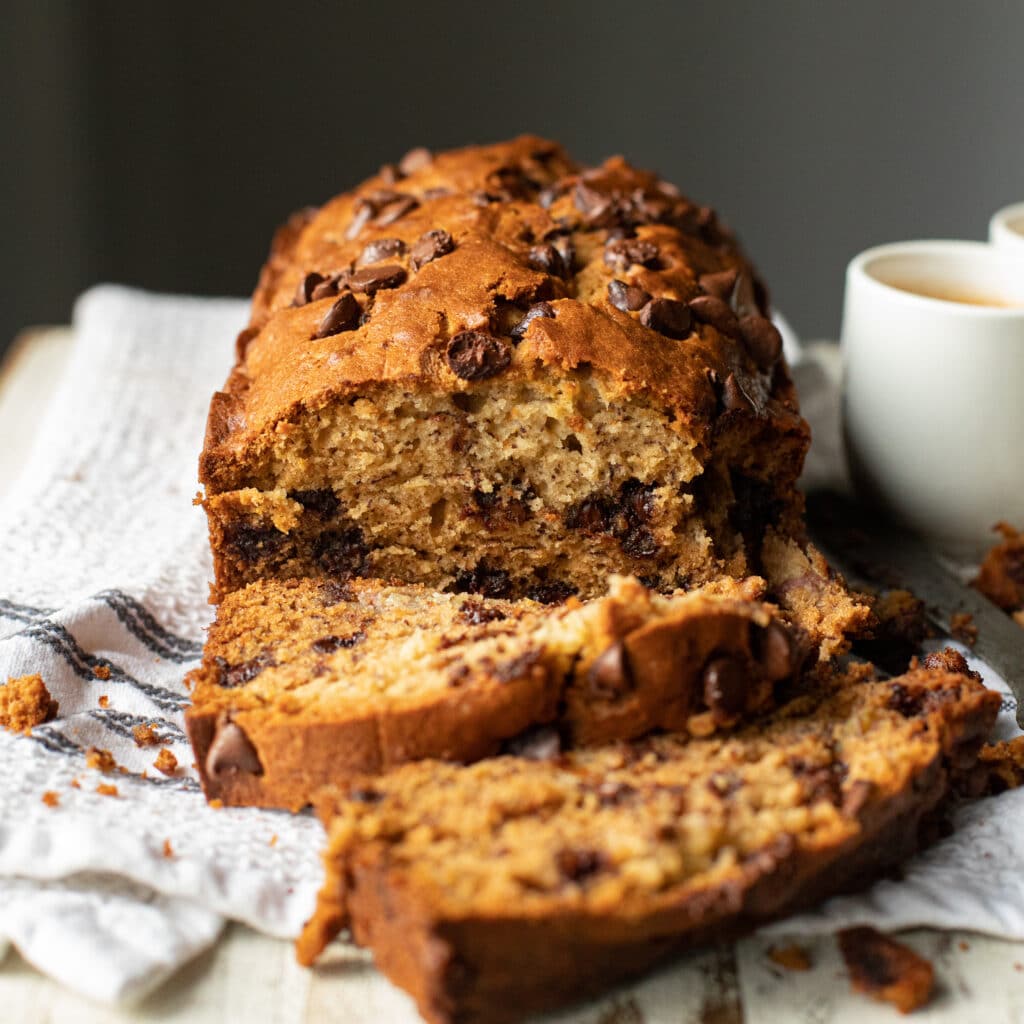 Chocolate Chip Banana Bread on a white towel with a white coffee cup on the side