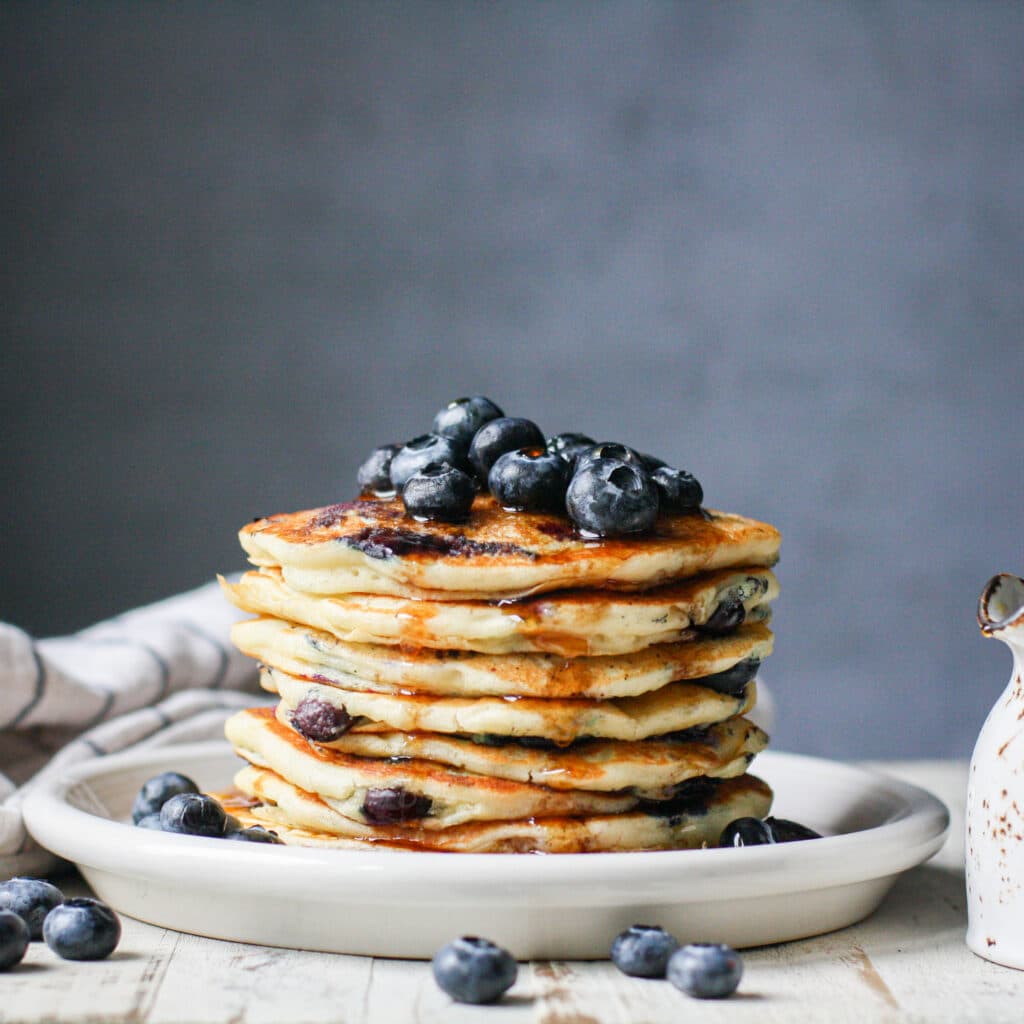 Vertical stack of blueberry pancakes with syrup on a white plate