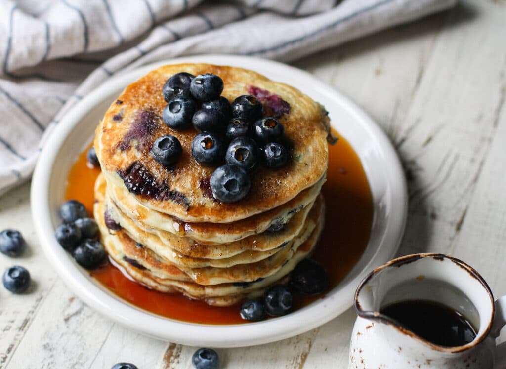 Overhead photo of blueberry pancakes on a white plate with syrup
