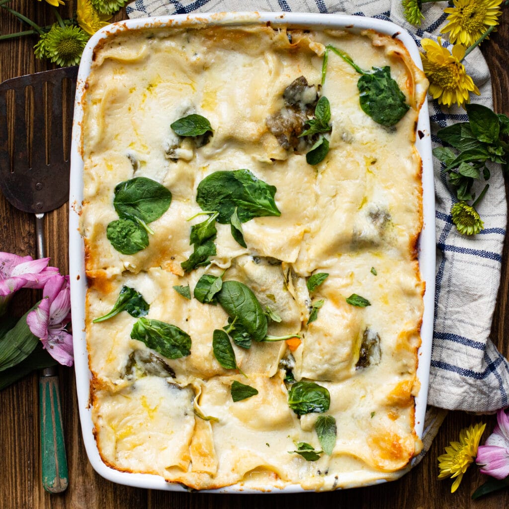 Rectangular white casserole dish with lasagna in a white sauce topped with spinach.