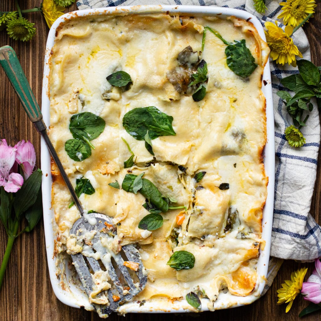 Large casserole dish of white lasagna, cut into squares with a spatula and spinach on top.