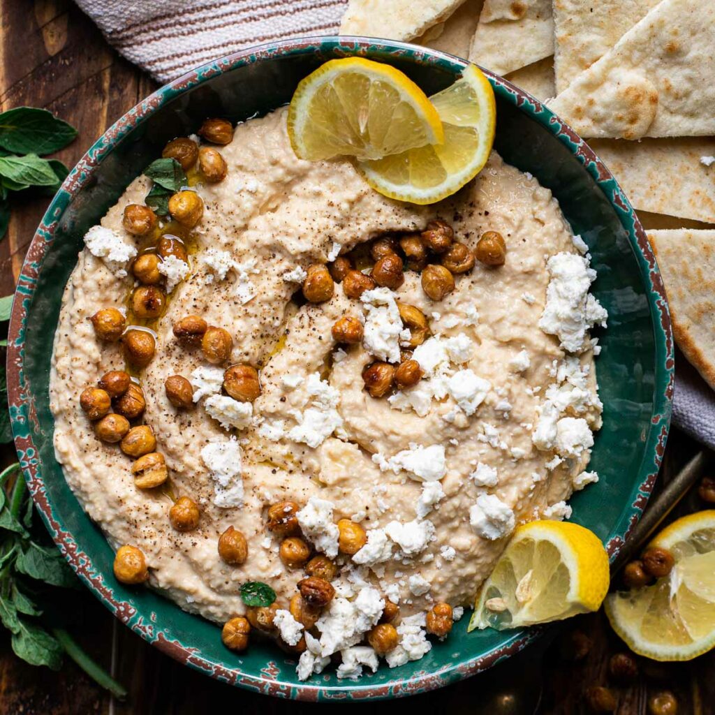 lemon hummus in a blue bowl garnished with feta cheese and crispy chickpeas