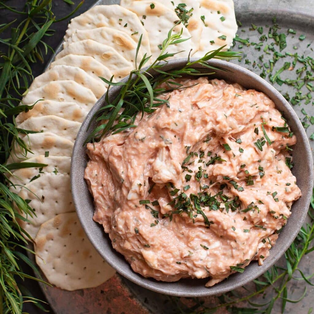 Cold Crab Dip in a bowl with water crackers and fresh tarragon