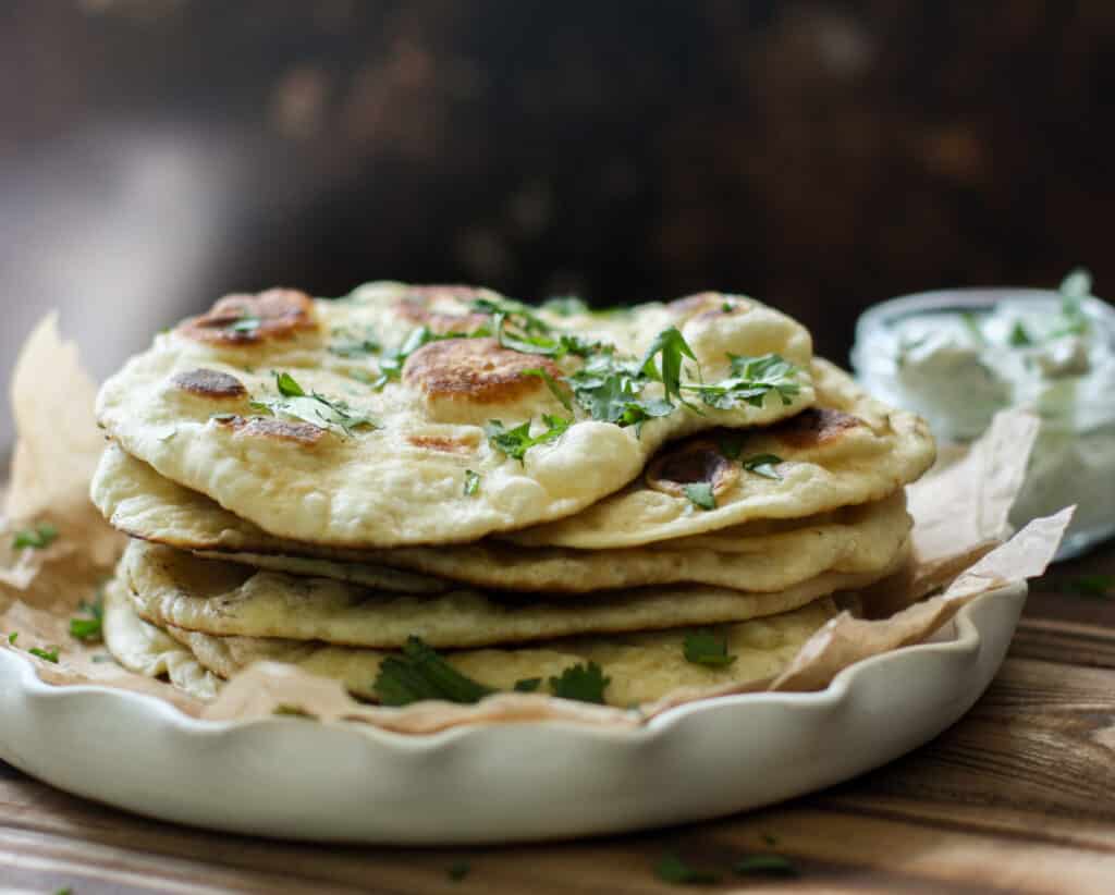Stack of naan on a white plate against a dark background