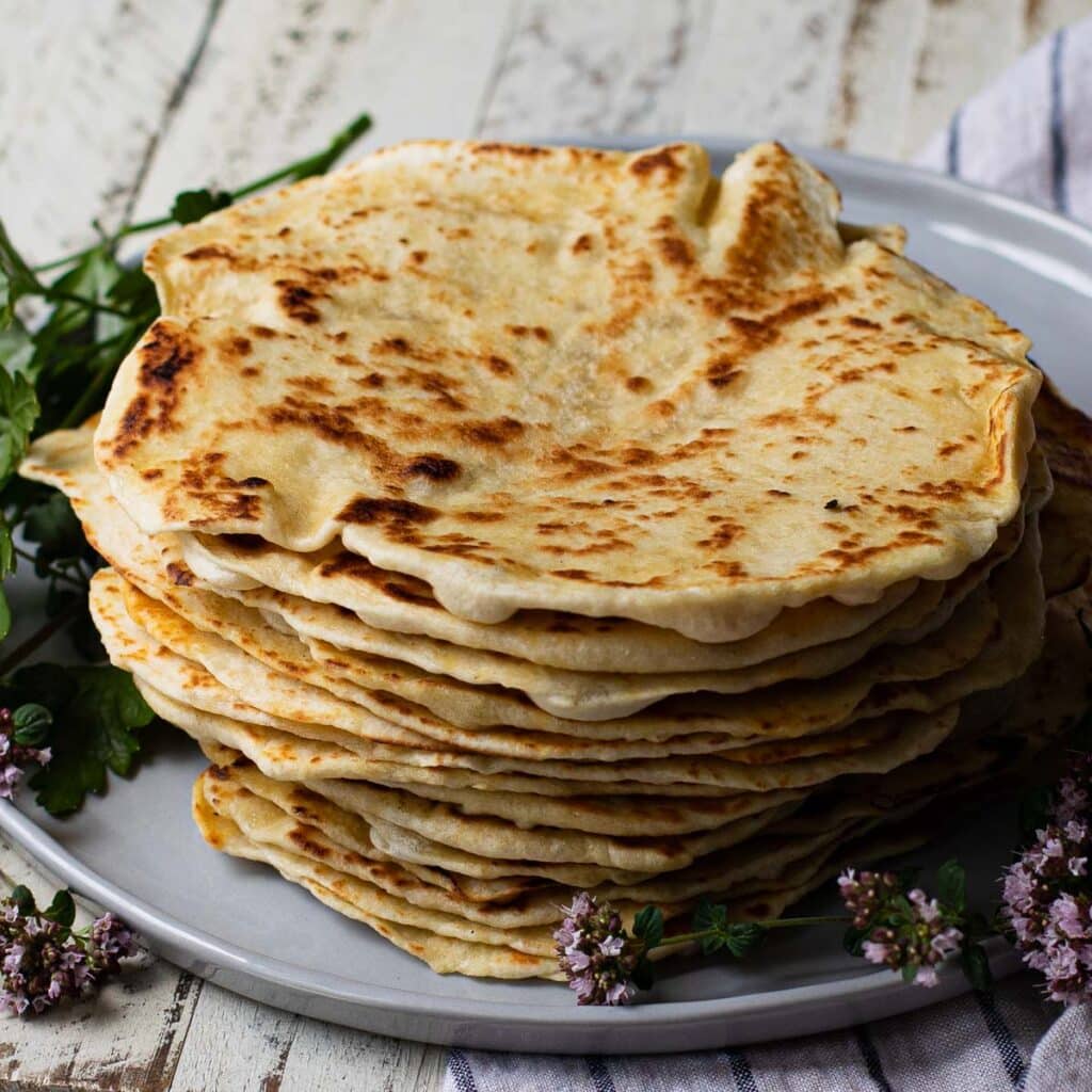A stack of Greek pita on a gray plate with oregano flowers