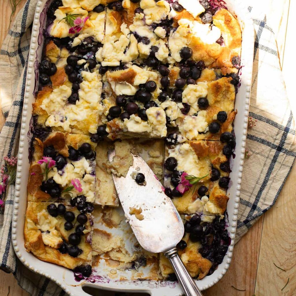 Blueberry bread pudding with cream cheese in a baking dish with a silver pie server