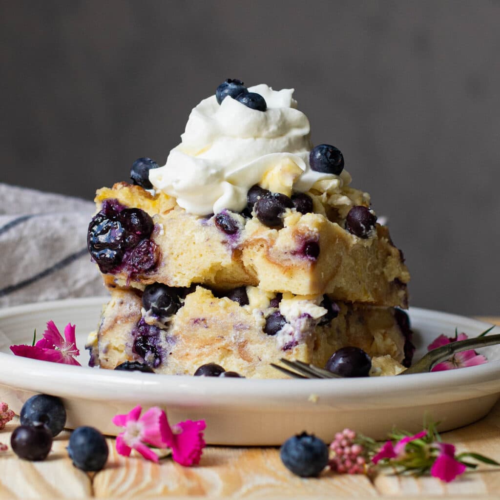 Slice of blueberry bread pudding topped with whipped cream