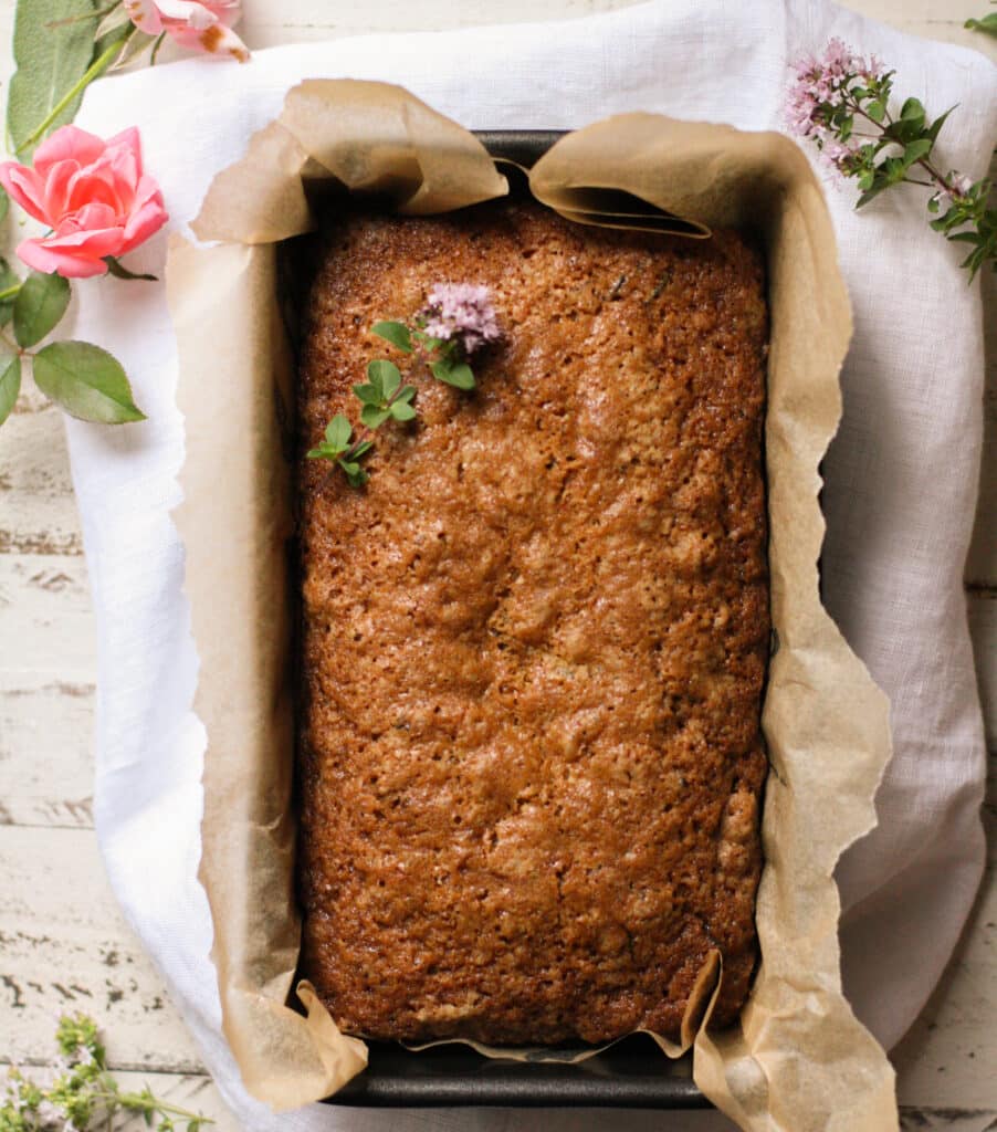 A baked loaf of Cinnamon Zucchini Bread in a loaf pan lined with parchment paper