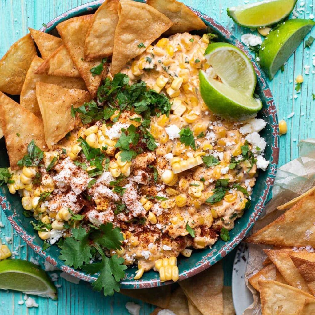 Elote Dip in a green bowl, garnished with cilantro and lime wedges