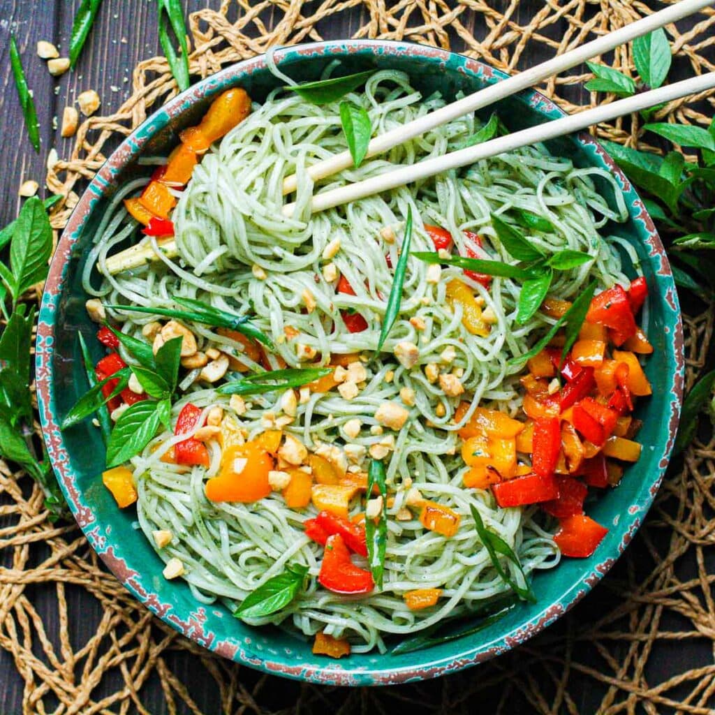 Thai Basil Pesto Noodles in a green bowl with chopsticks and chopped bell peppers