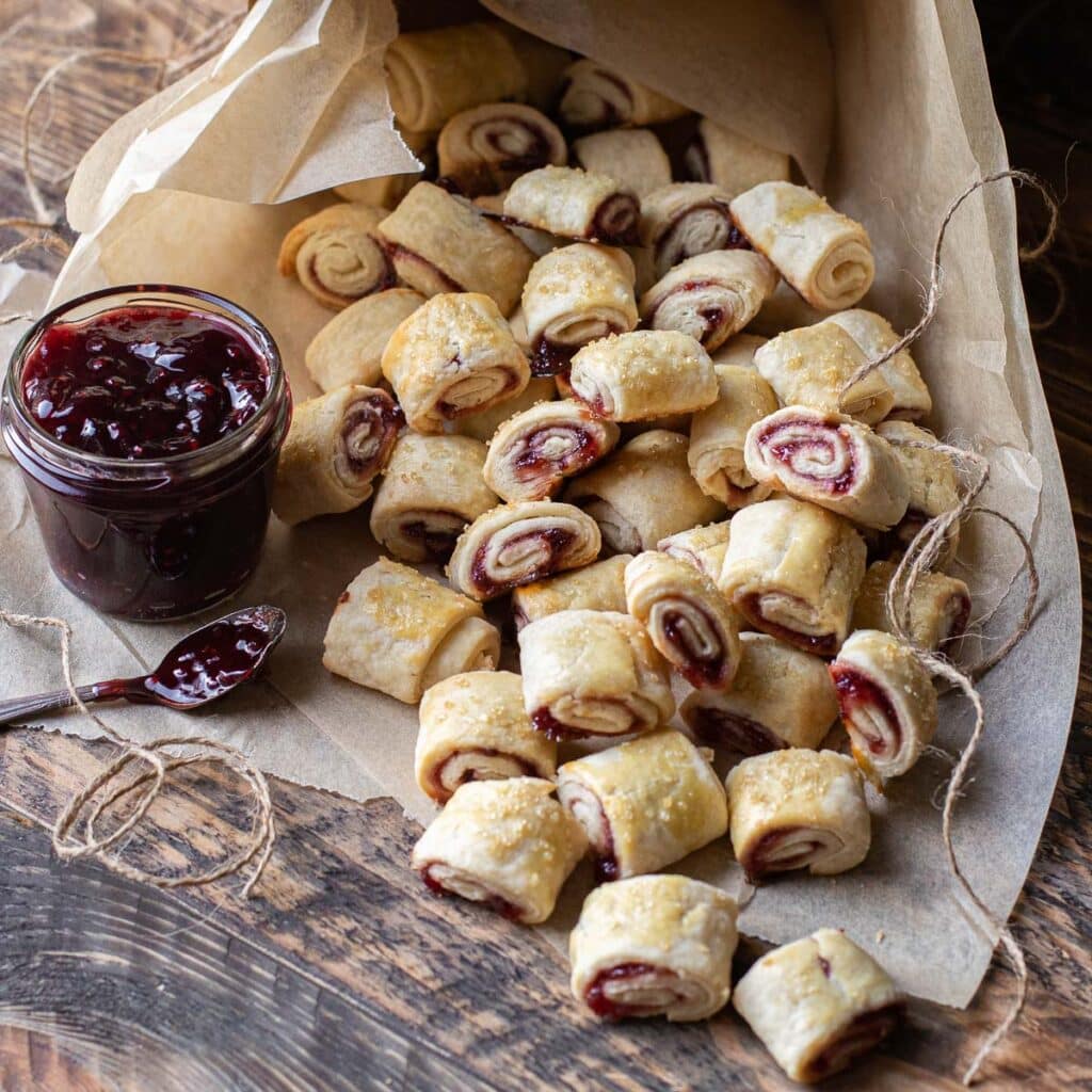 Raspberry Rugelach on brown parchment paper with a jar of raspberry jam on the side
