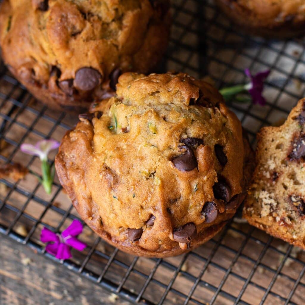 chocolate chip zucchini muffins on a cooling rack, garnished with small purple flowers