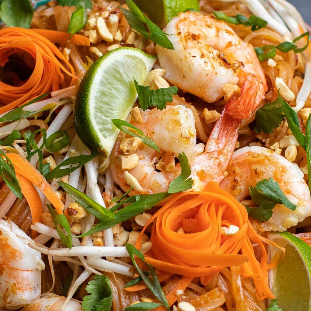 close up view of shrimp pad thai with cilantro, scallions and carrots