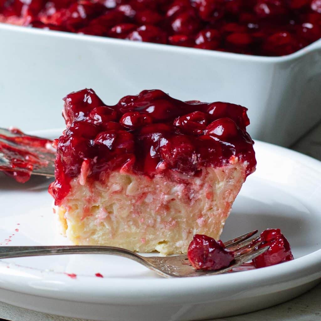 One slice of kugel on a white plate, topped with cherries