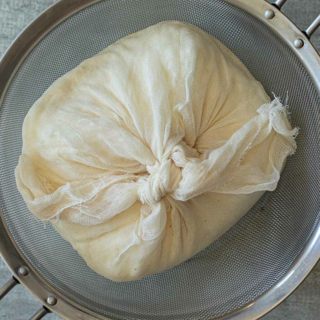 Overhead view of yogurt wrapped in cheesecloth in a mesh strainer