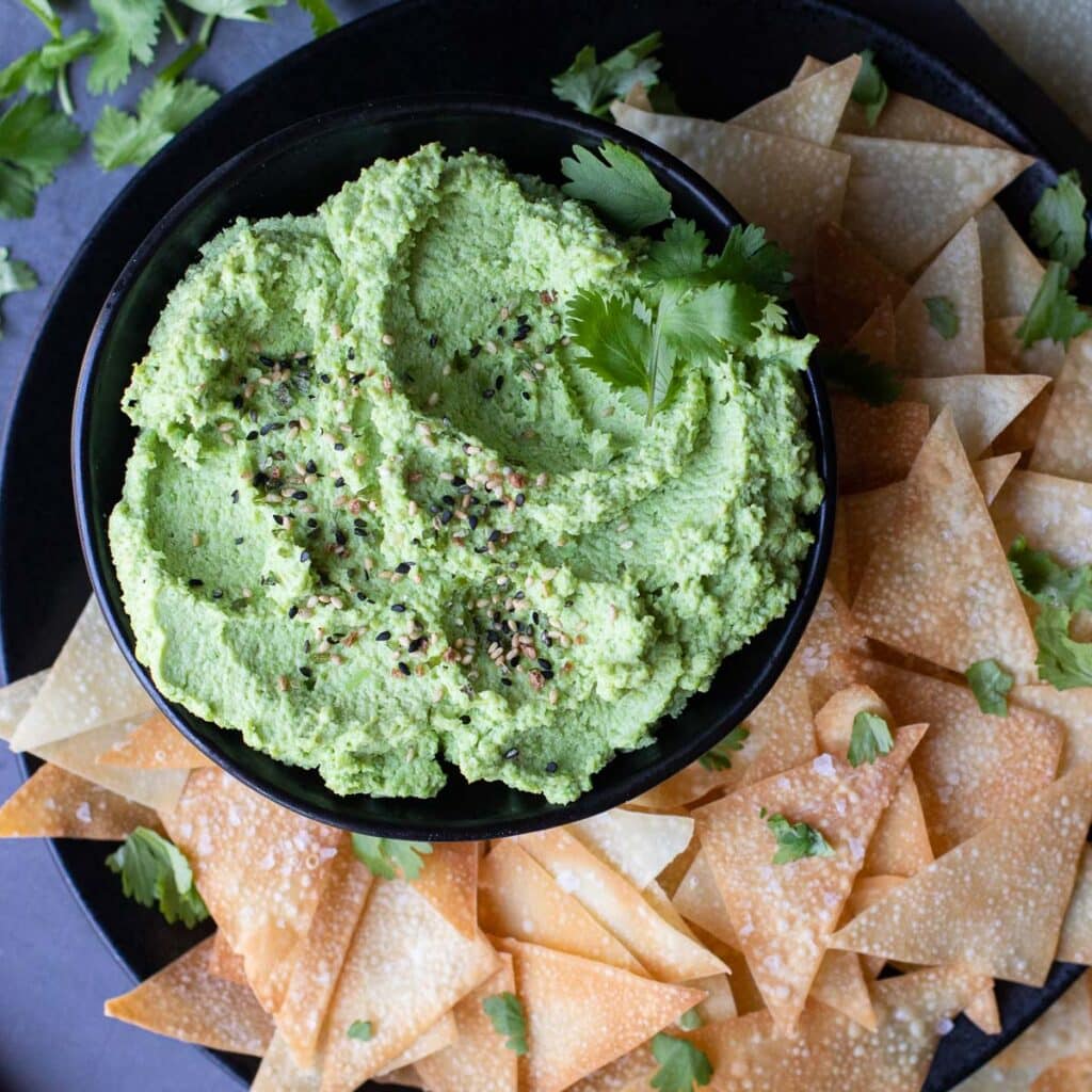 vegan edamame hummus in a black bowl with homemade wonton chips on the side