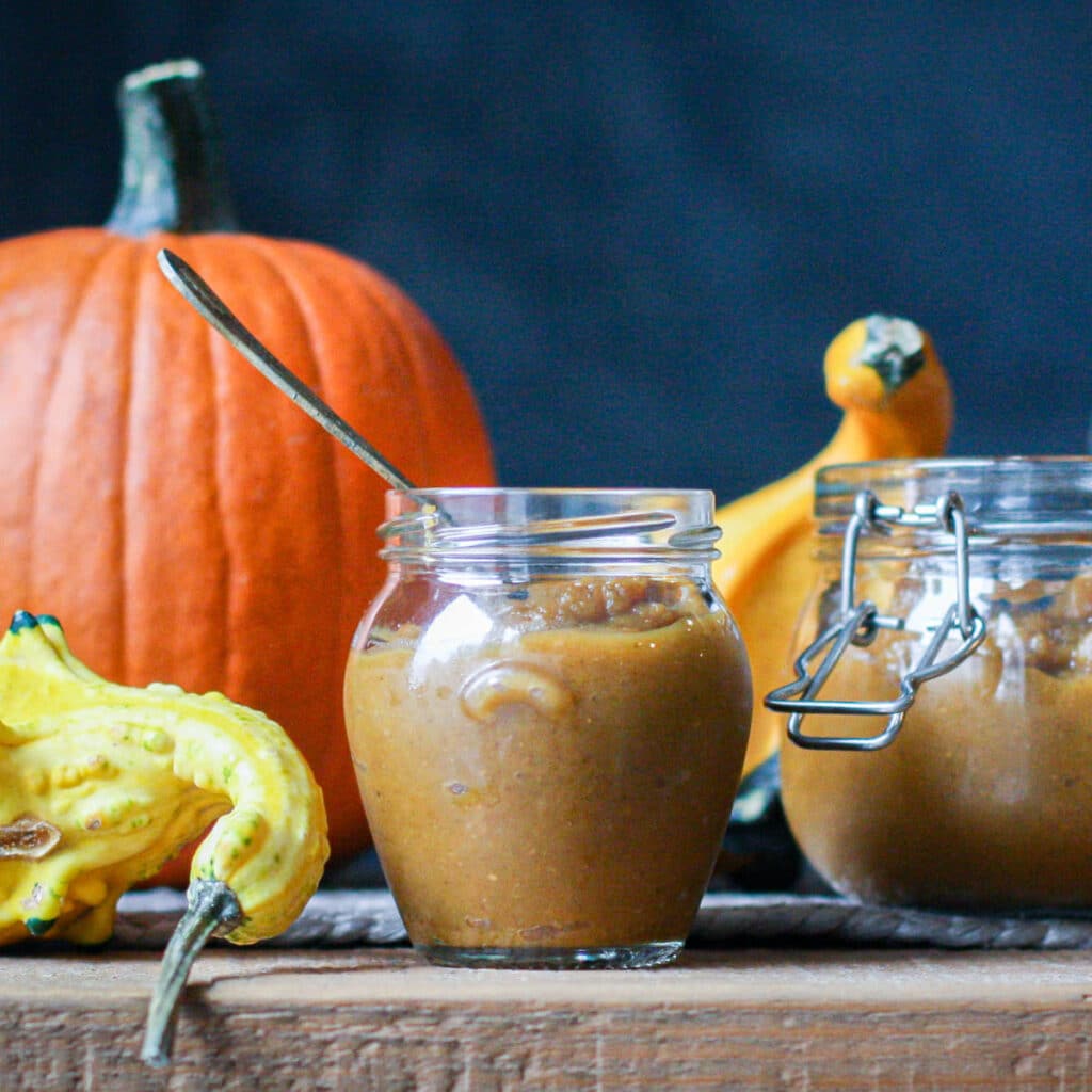 homemade pumpkin butter in a glass jar with pumpkins in the background