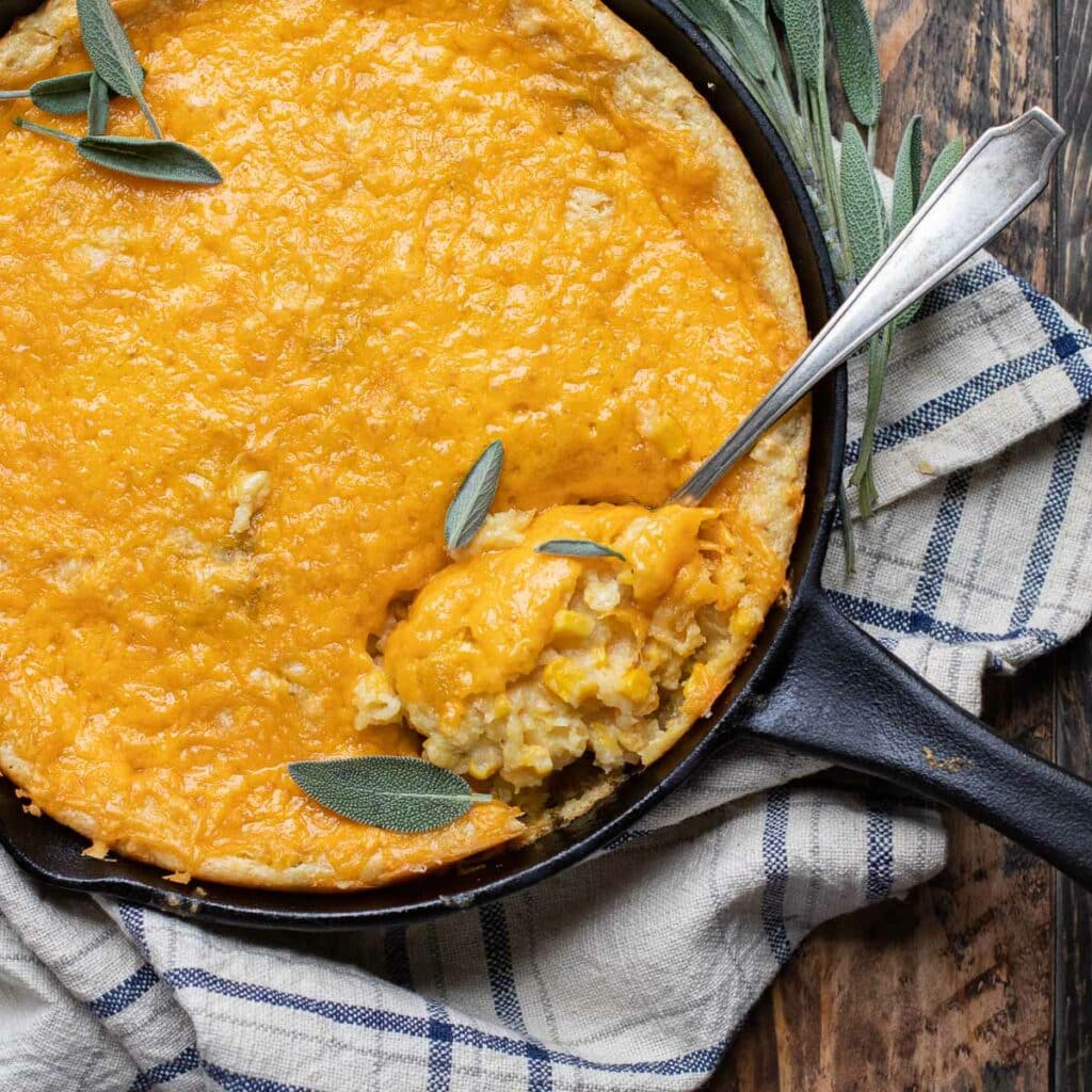 Jalapeño Corn Casserole in a black skillet with a serving spoon and fresh sage leaves