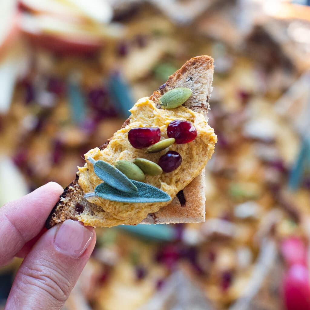 A piece of cinnamon toast topped with pumpkin butter, pumpkin seeds, pomegranate arils and sage leaves