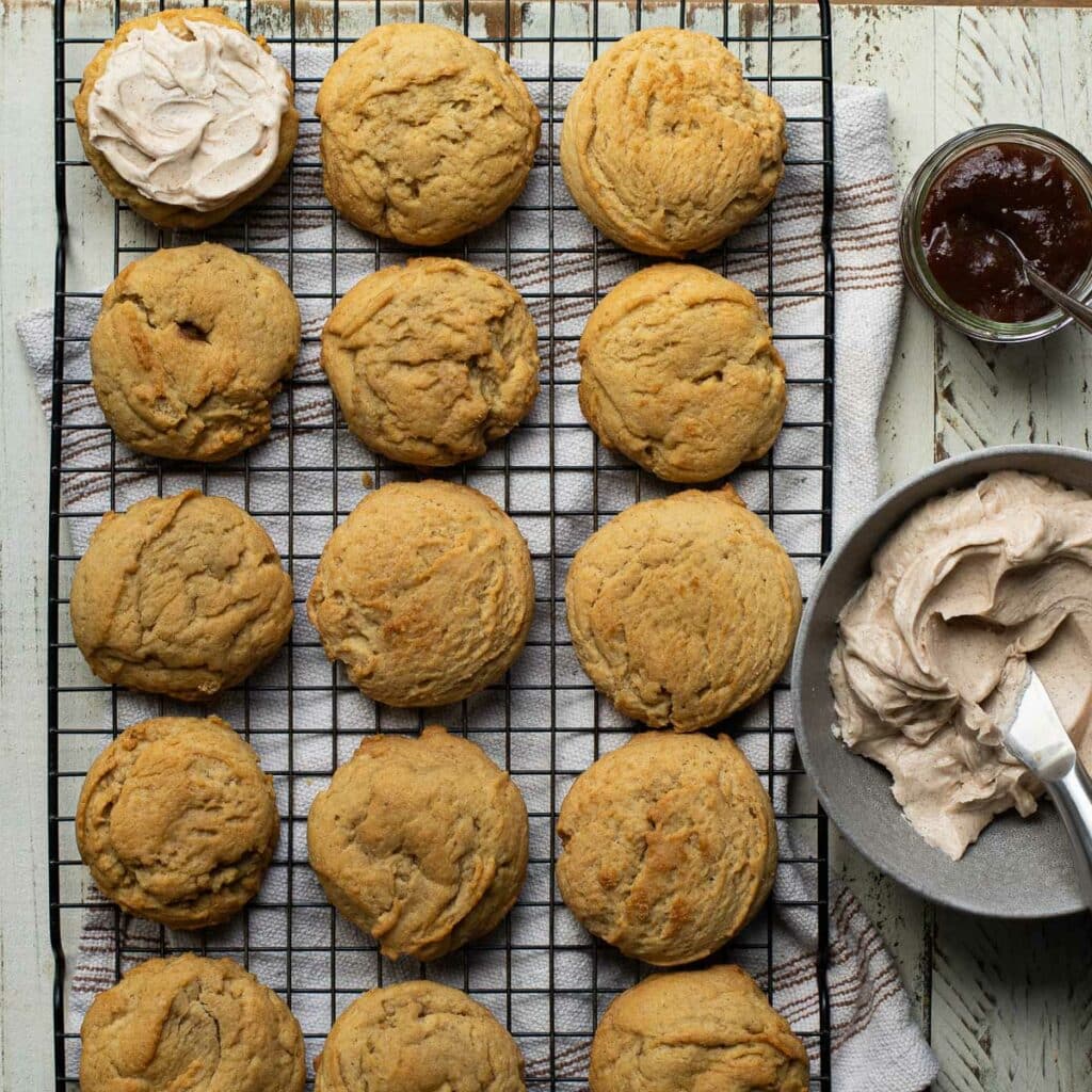 unfrosted apple butter cookies on a wire cooling rack with bowls of apple butter and frosting on the side