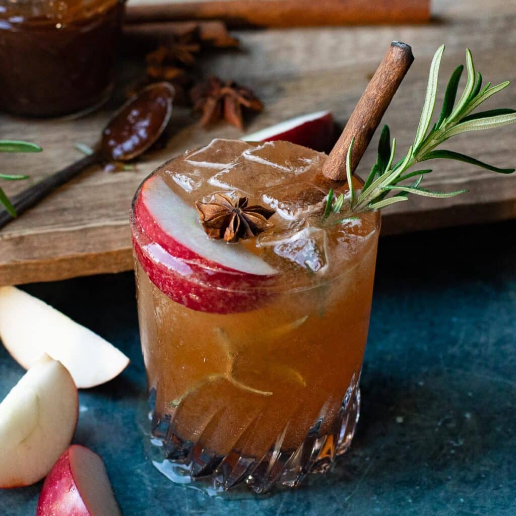 Apple Butter Vodka Cocktail in a rocks glass with an apple wedge, cinnamon stick, sprig of rosemary and star anise