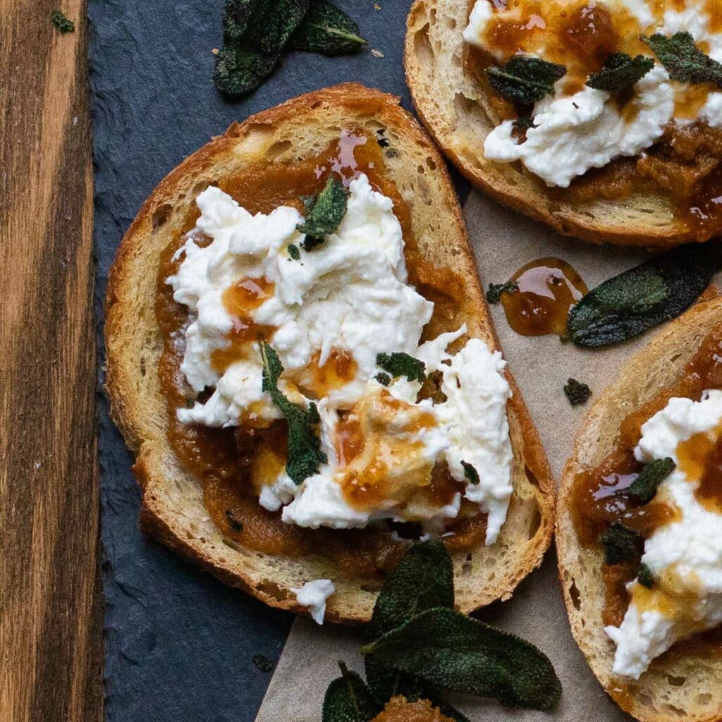 A piece of burrata toast drizzled with fig syrup and garnished with sage leaves