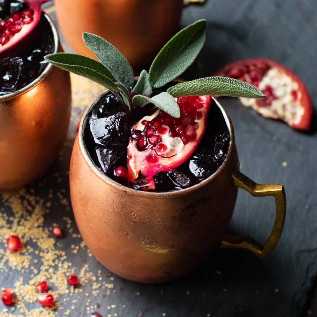 Moscow Mule in a copper mug with a slice of pomegranate and fresh sage leaves