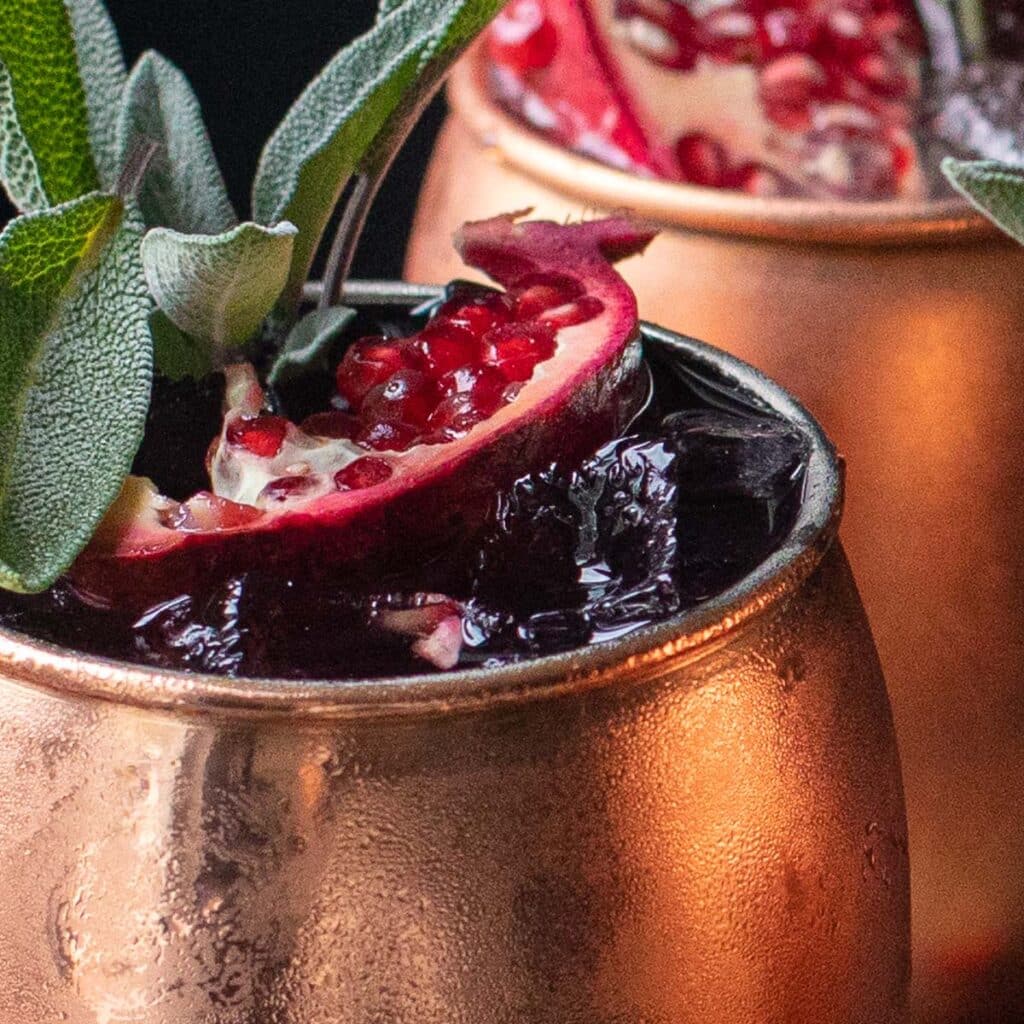 The top of a mule mug with pomegranate and fresh sage leaves