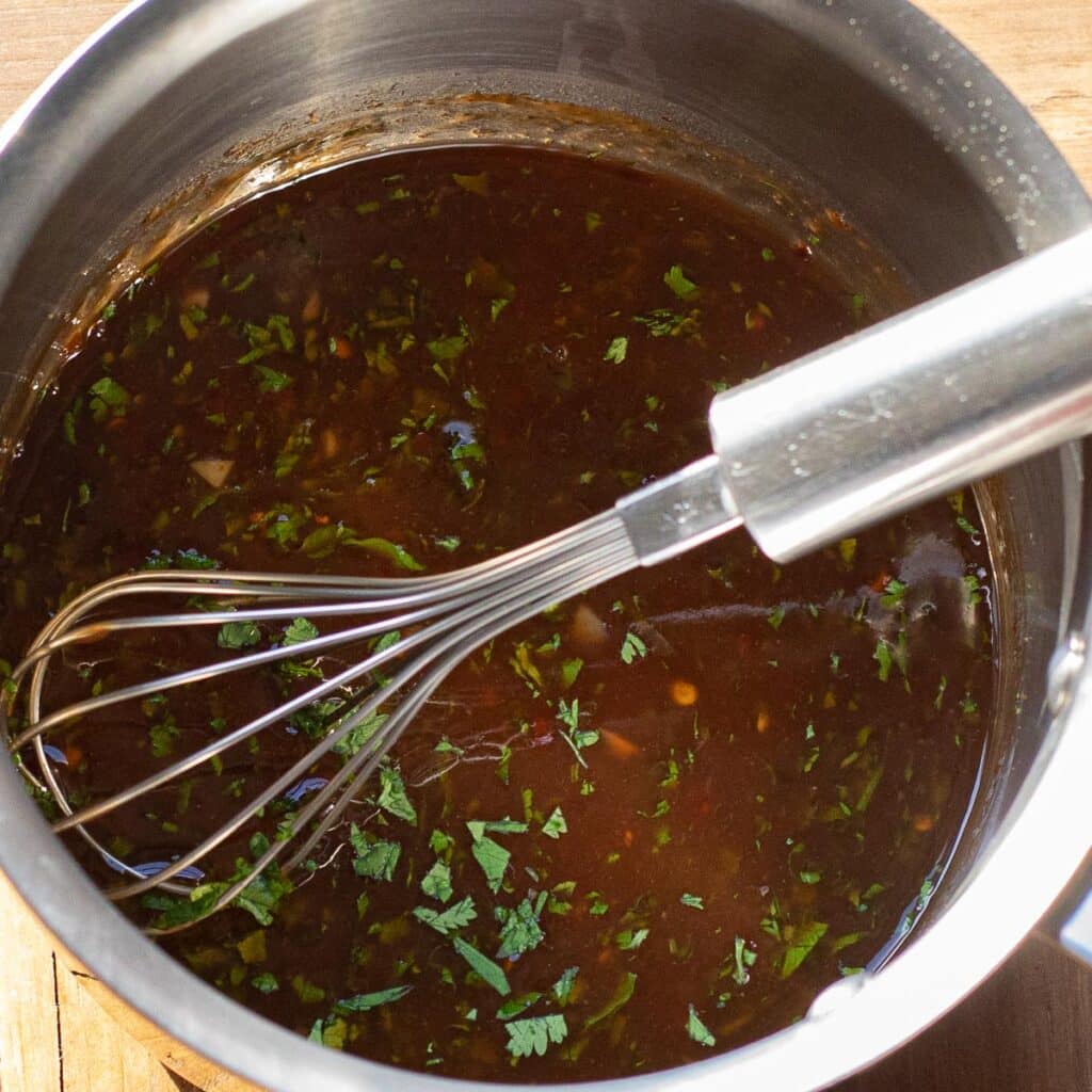 Plum sauce in a stainless steel saucepan with a wire whisk