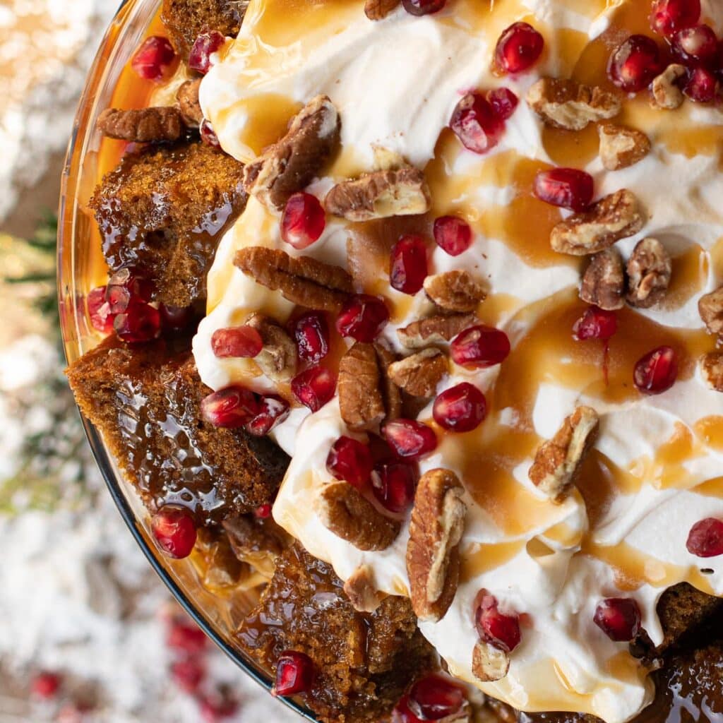 Whipped cream on top of gingerbread cake topped with pomegranate seeds and chopped pecans
