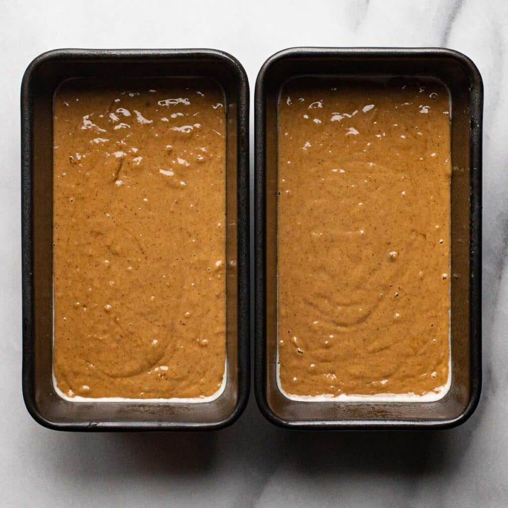 Two loaf pans fill with gingerbread cake batter