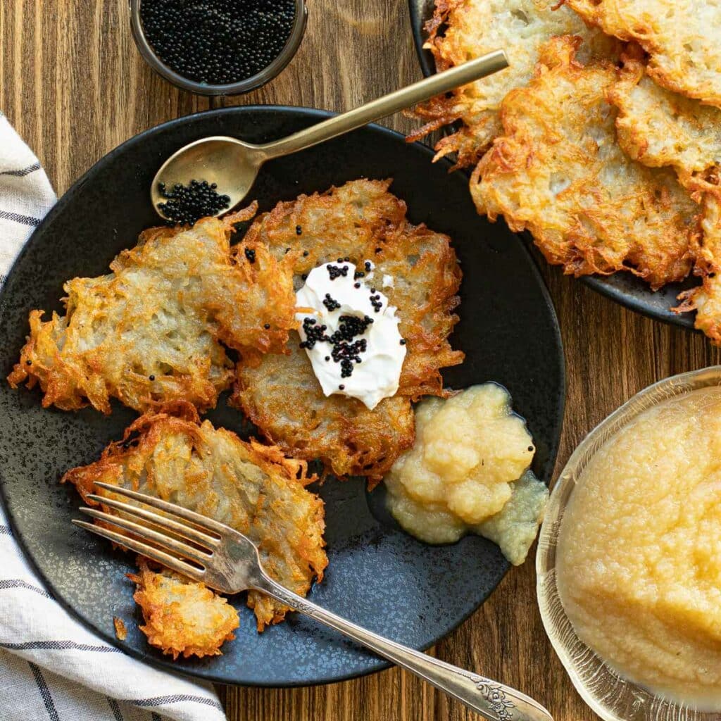 Latkes on a black plate with sour cream, caviar and applesauce