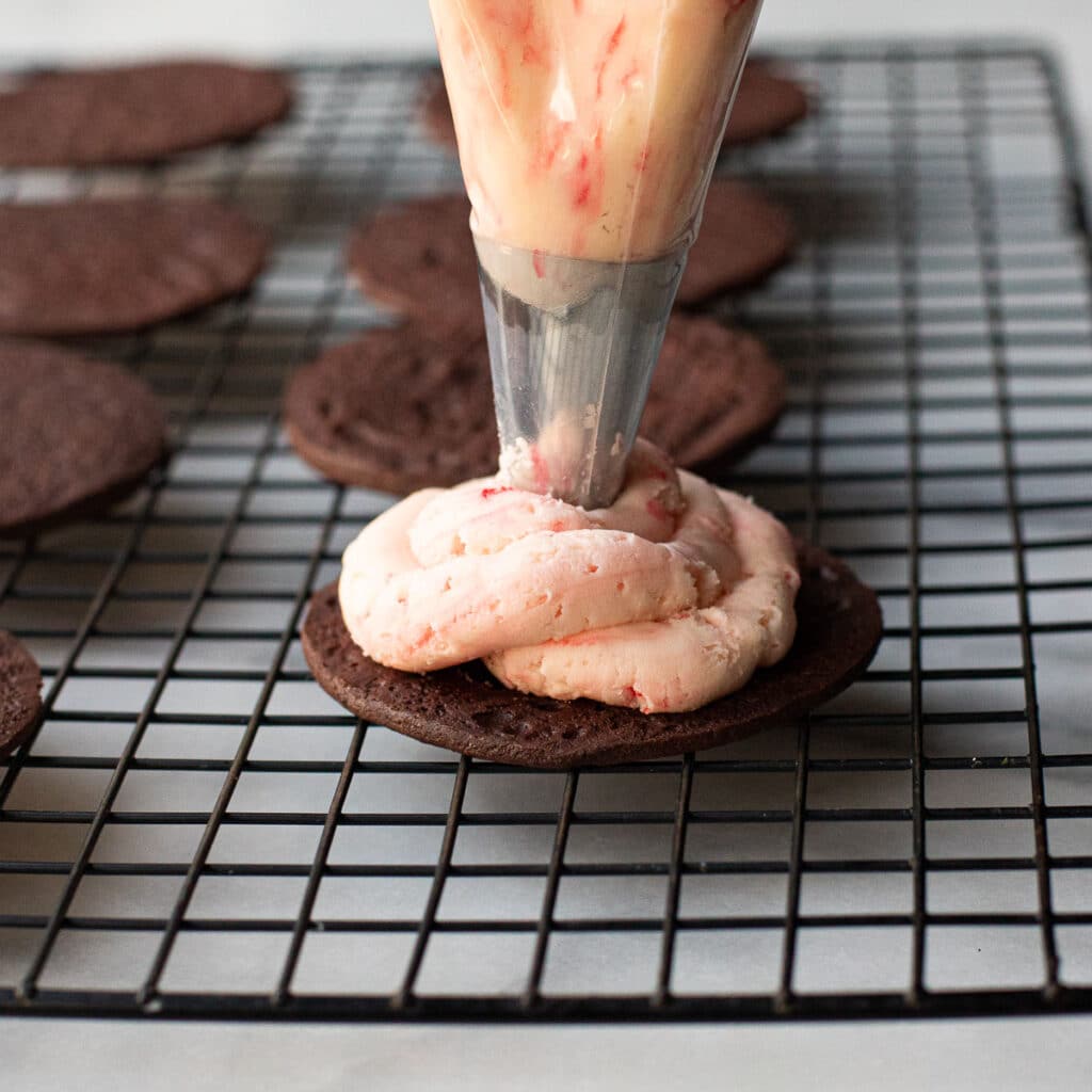 Peppermint cream filling being piped onto a chocolate cookie