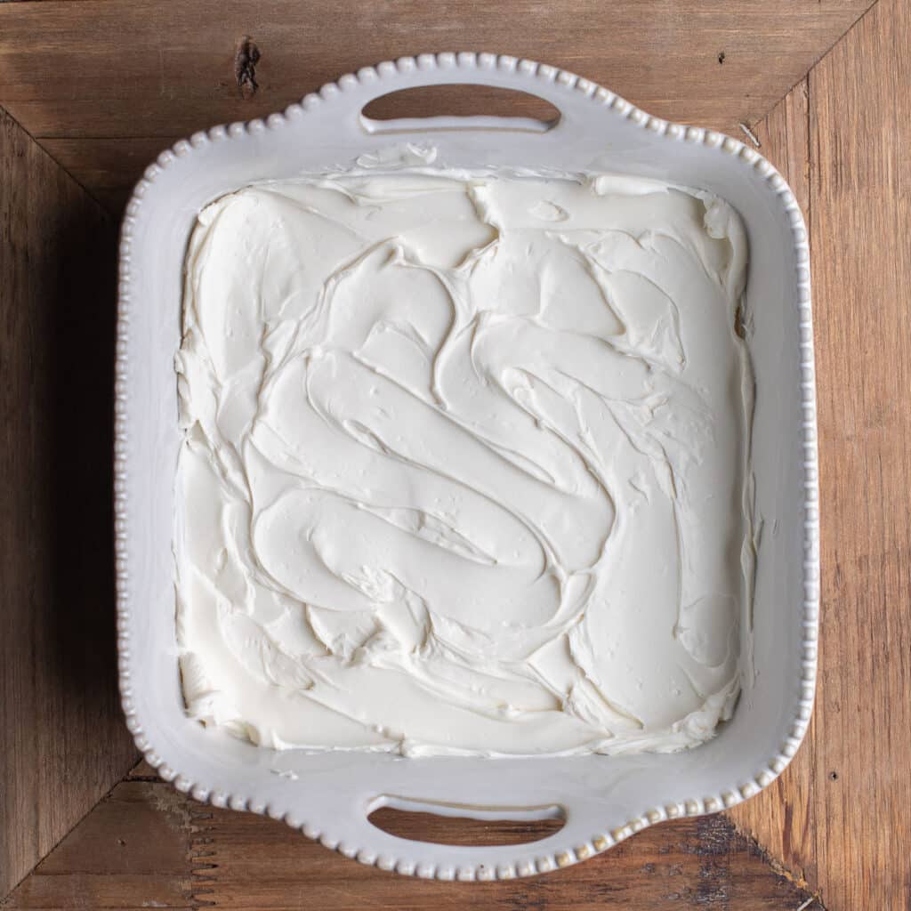 Cream cheese spread across the bottom of a white baking dish