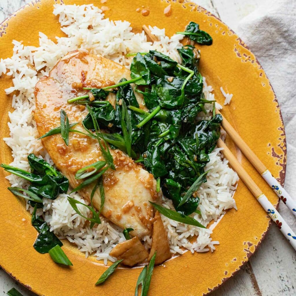 Asian tilapia and spinach over a bed of white rice with chopsticks