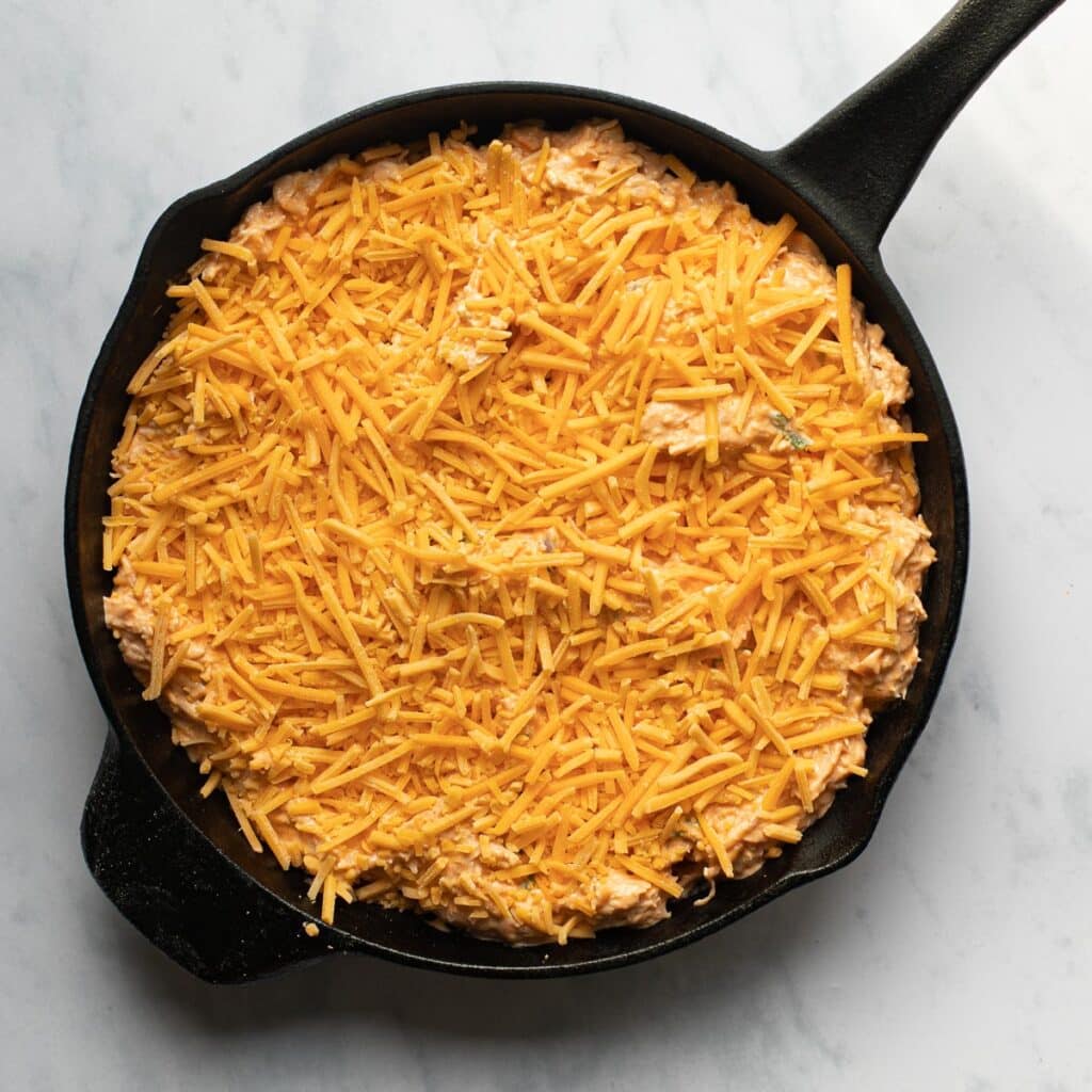 cold buffalo chicken dip with grated cheddar cheese on top, before baking