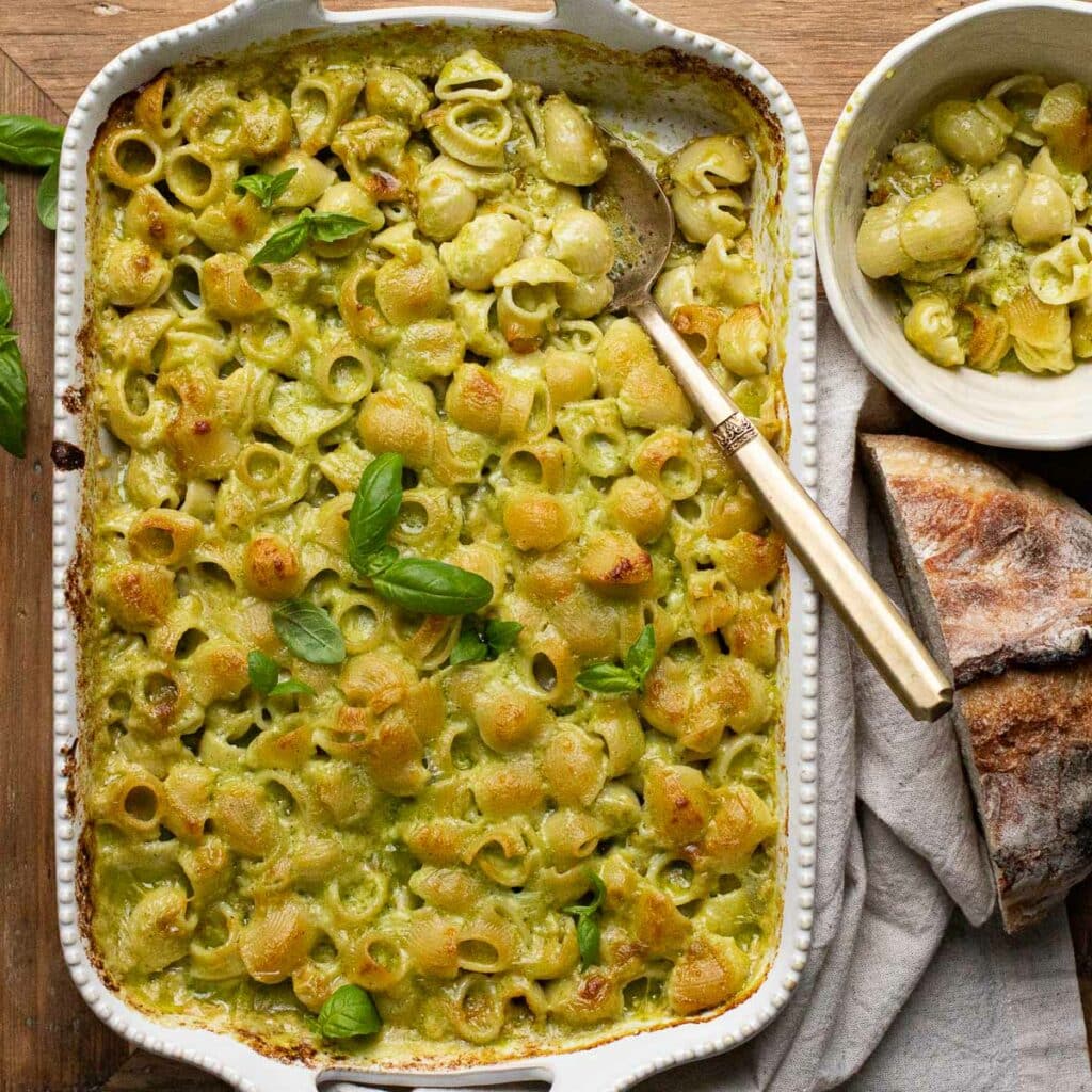 Cheesy Baked Pesto Pasta Recipe in a white baking dish with a gold serving spoon