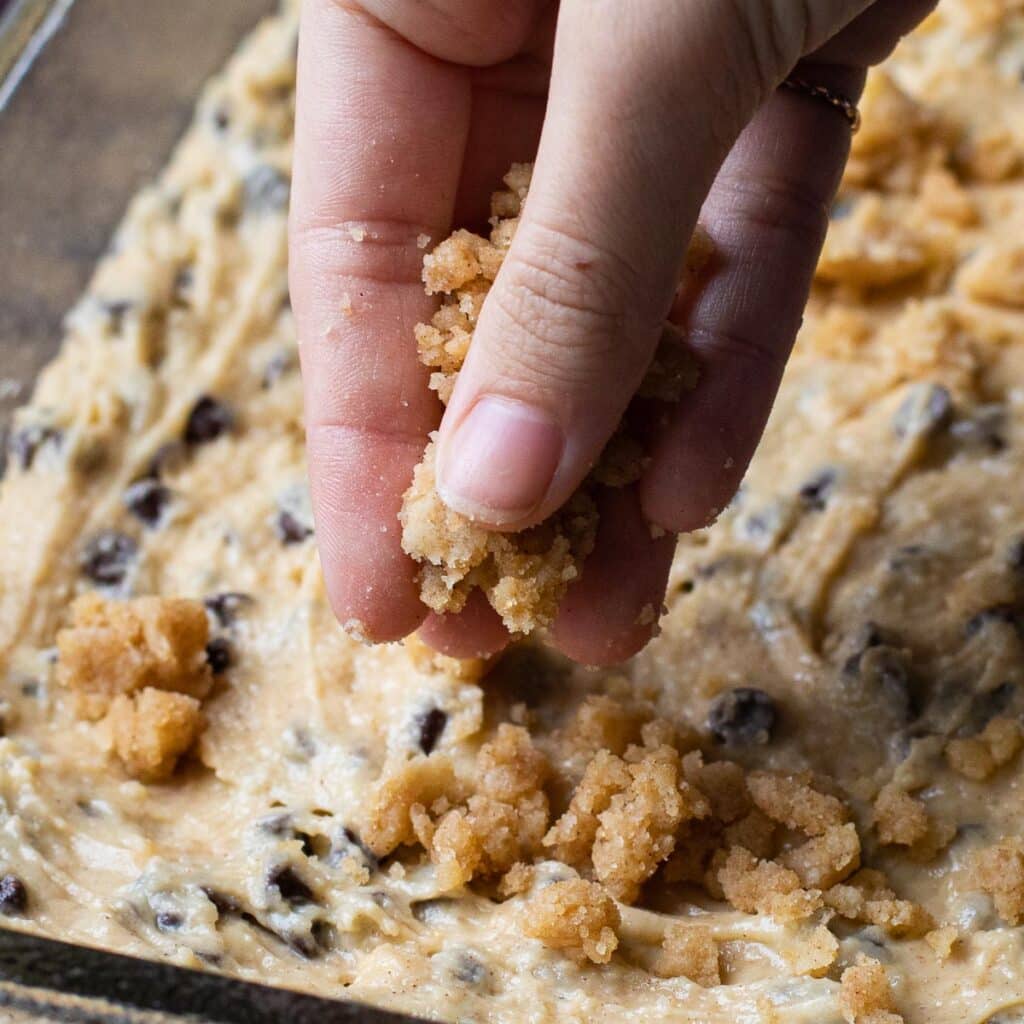 A hand placing streusel topping onto cake batter in a pan