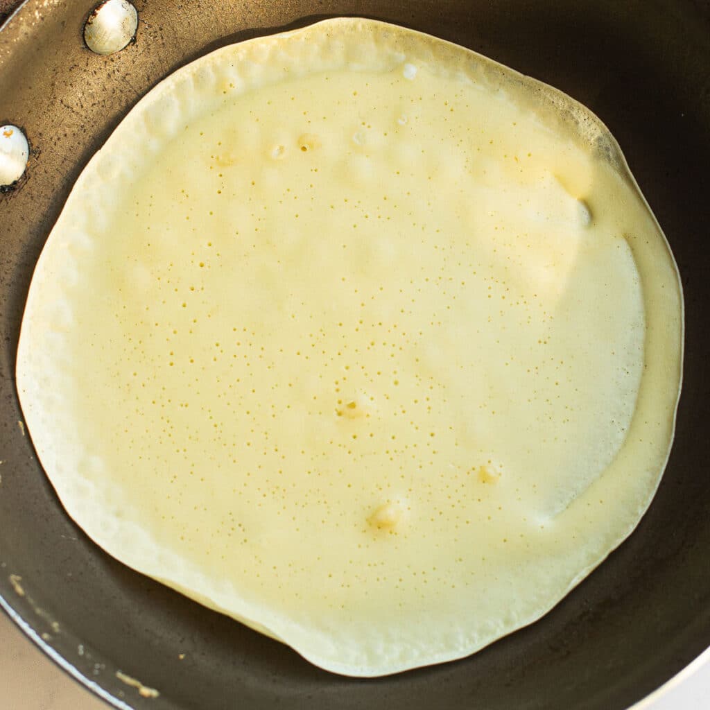 A crepe cooking in a pan with the edges curling up