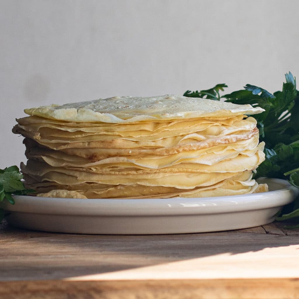 Homemade crepes stacked up on a white plate