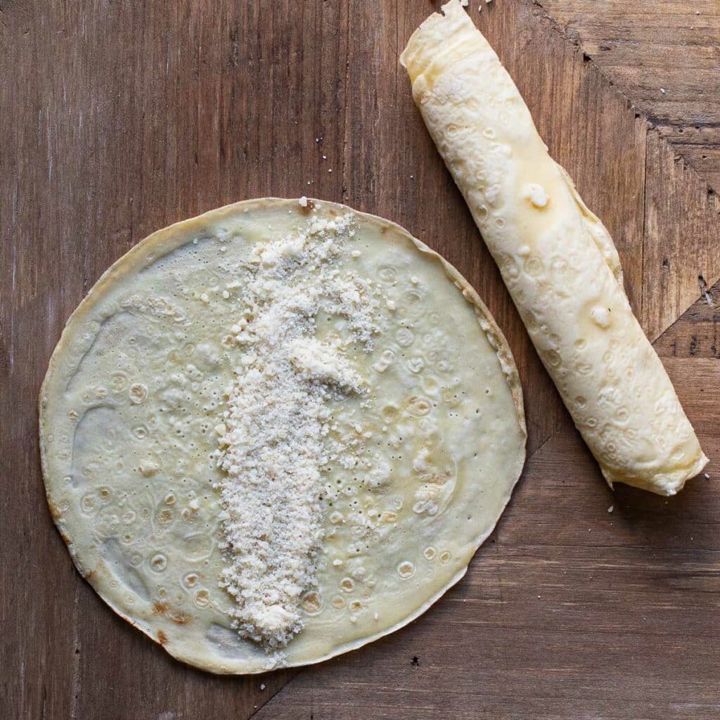 Parmesan cheese sprinkled onto the center of a crepe next to a rolled crepe