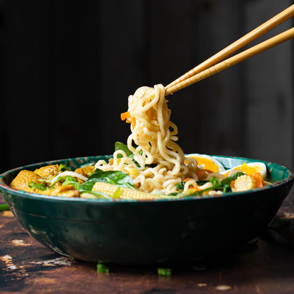 Chopsticks holding ramen noodles over a bowl of soup