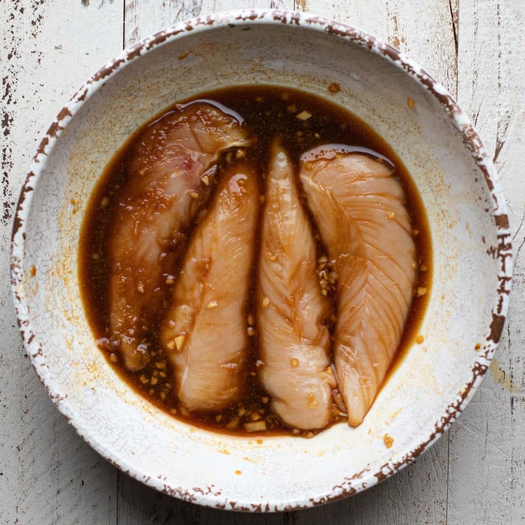 Slices of raw chicken marinating in soy sauce and garlic