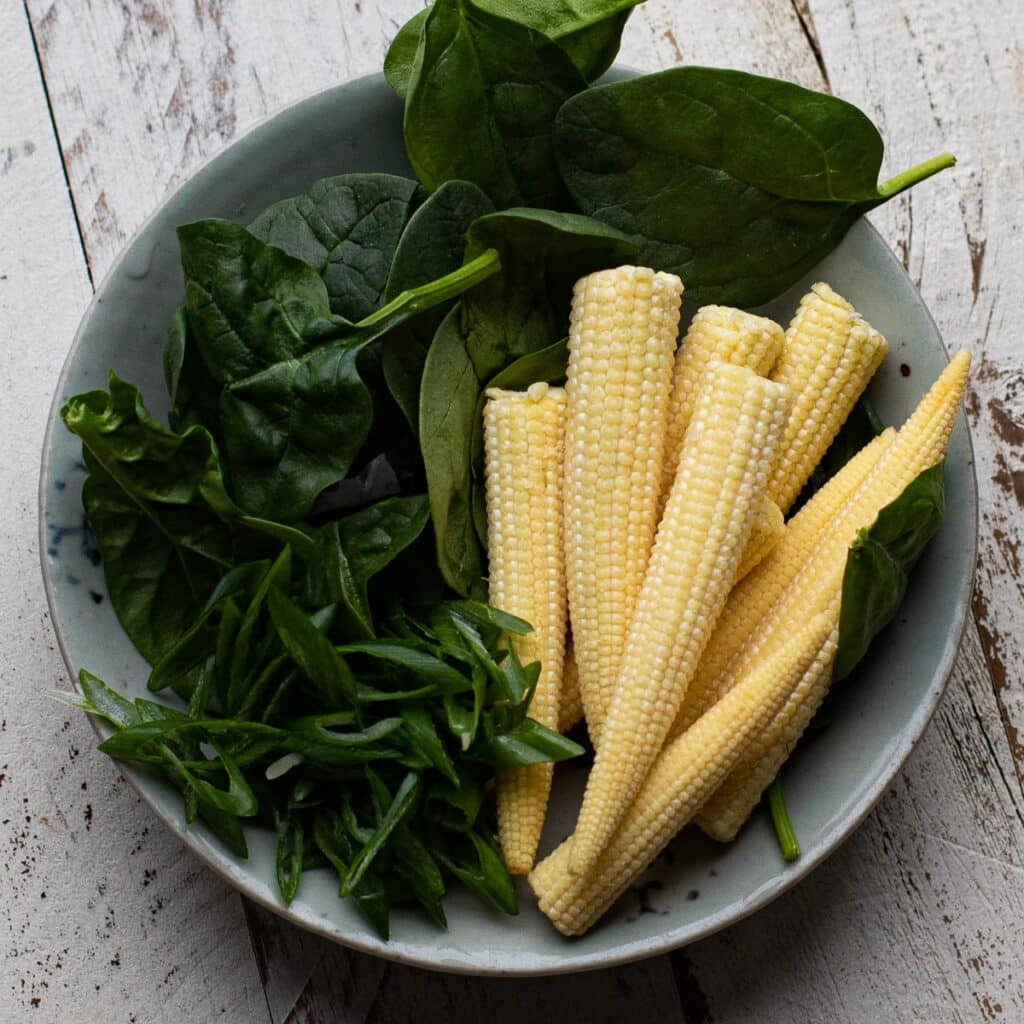 Baby corn, baby spinach and chopped scallions arranged in a small bowl