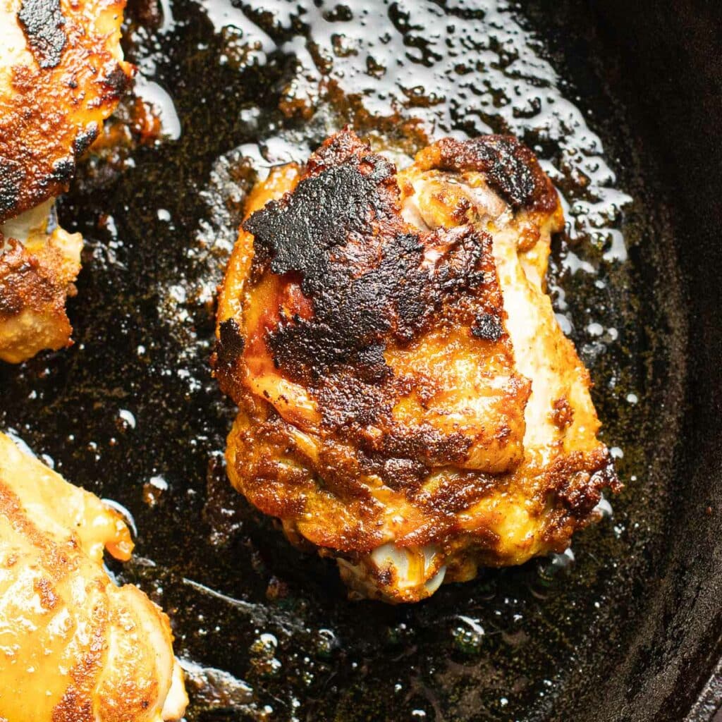 A seasoned chicken thigh cooking in a cast iron skillet