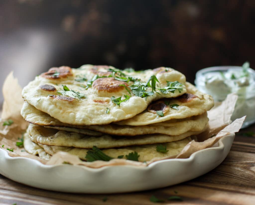 Naan bread stacked up on a white serving plate
