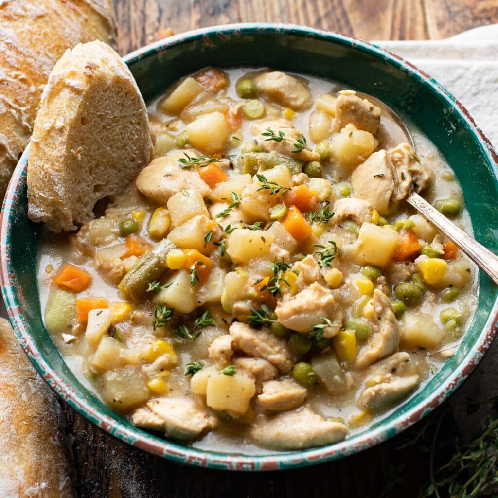 old fashioned chicken and vegetable stew with a piece of bread dipped in