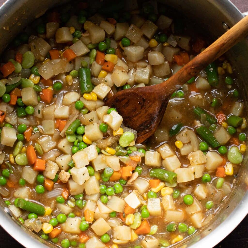 Cubed potatoes, peas, carrots, green beans and corn cooking in a pot